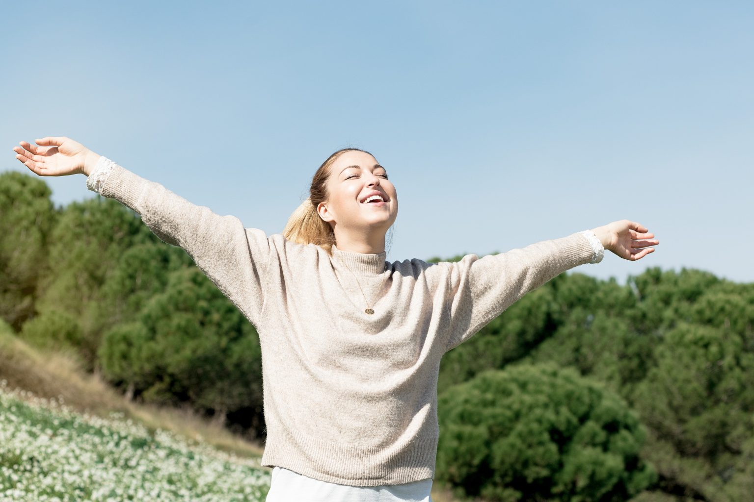 Confident woman with open arms enjoying nature, symbolizing freedom and body awareness.