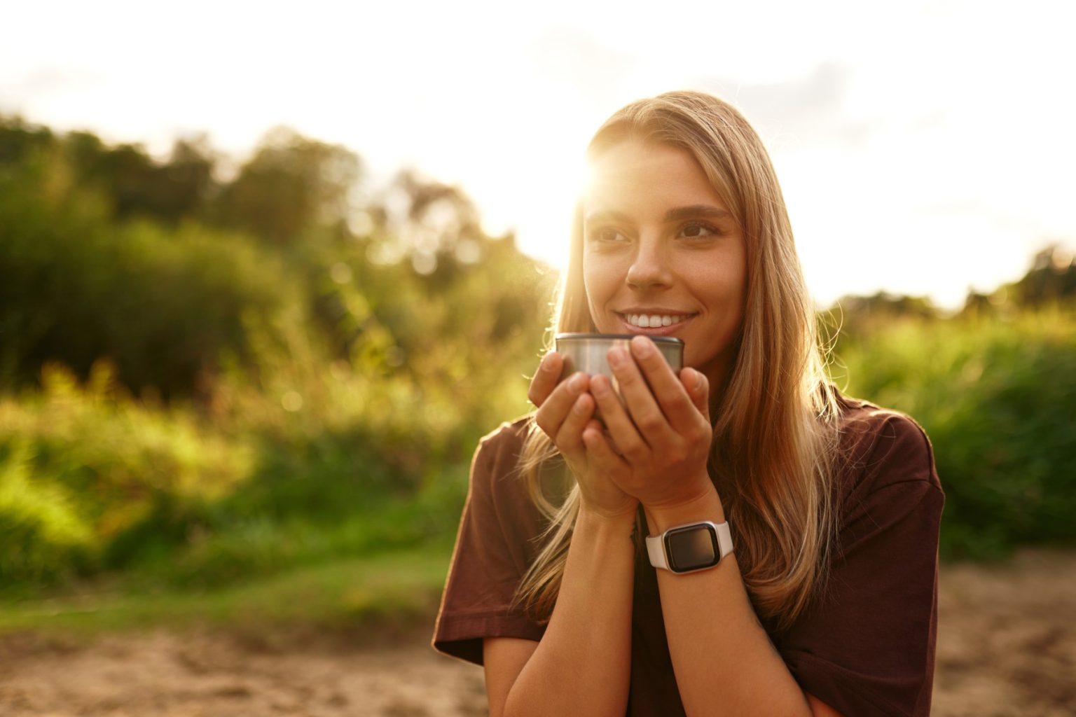 Smiling woman enjoying a mindful moment with herbal tea in warm sunlight, representing a balanced modern lifestyle.