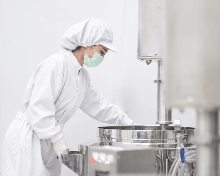 Technician in protective clothing working at a stainless-steel processing vessel